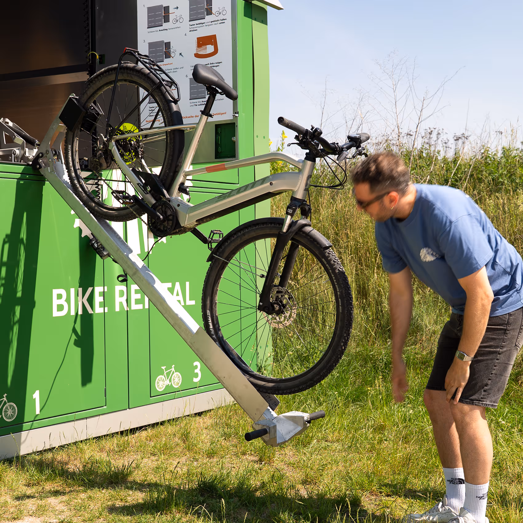 Mann entnimmt E-Bike aus der automatisierten Verleihbox auf einem Feldweg